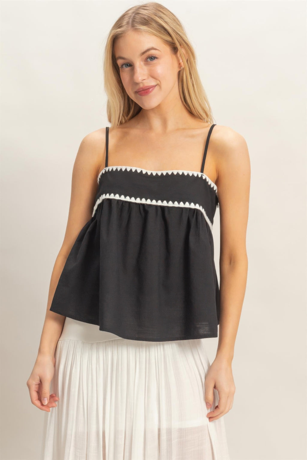 Black sleeveless babydoll top with white zigzag trim and gathered ruffle neckline