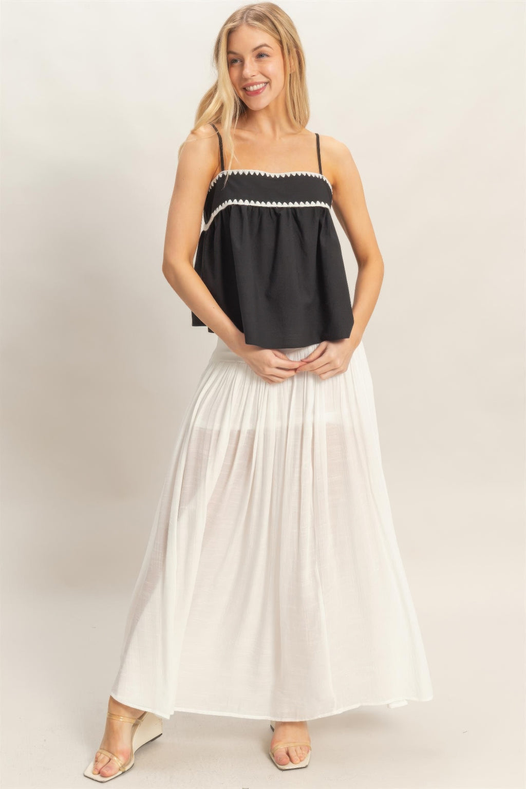 Black sleeveless babydoll top with scalloped white trim and loose tiered fit