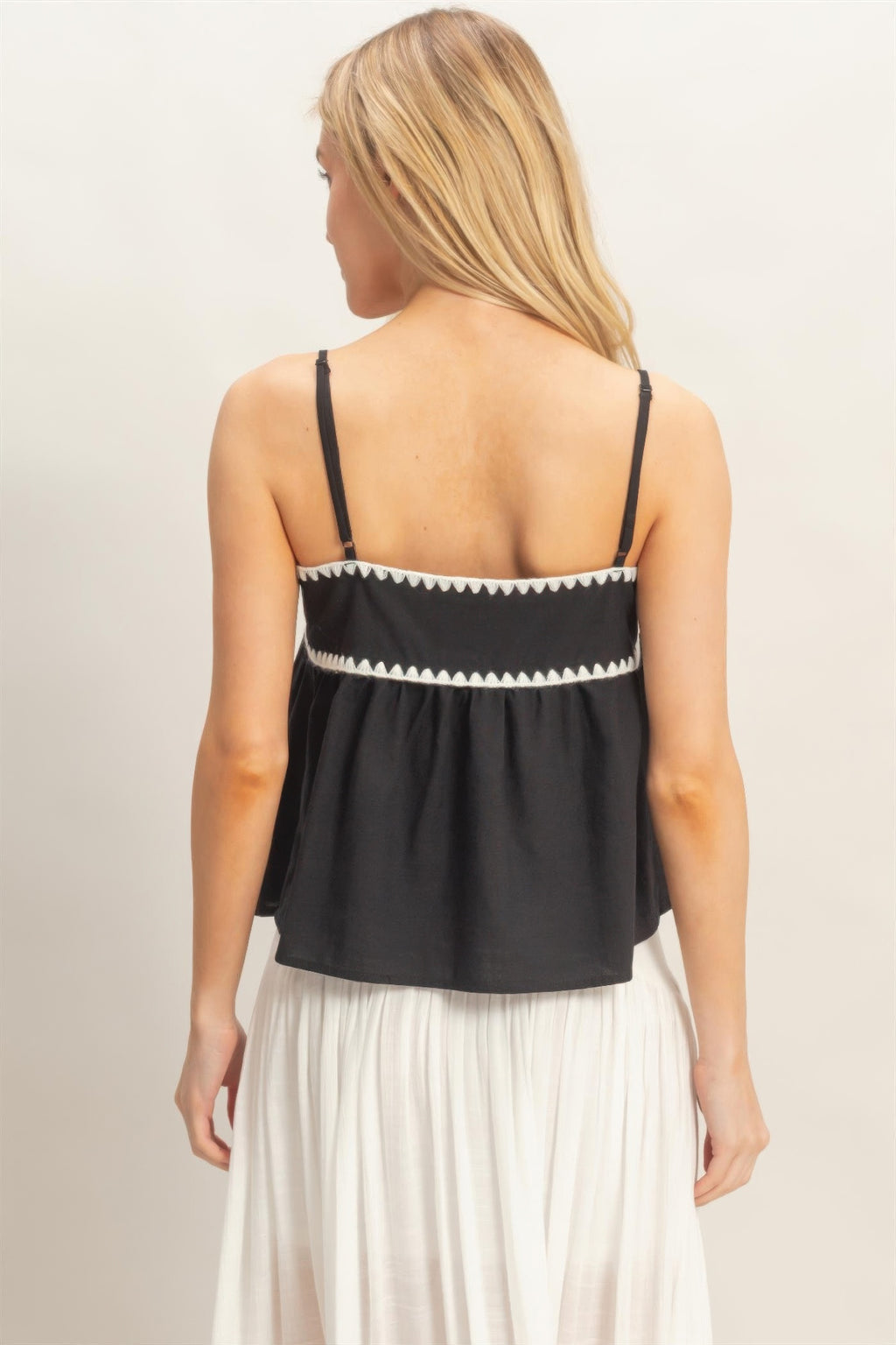 Back view: black sleeveless babydoll top with thin straps and white zigzag trim band