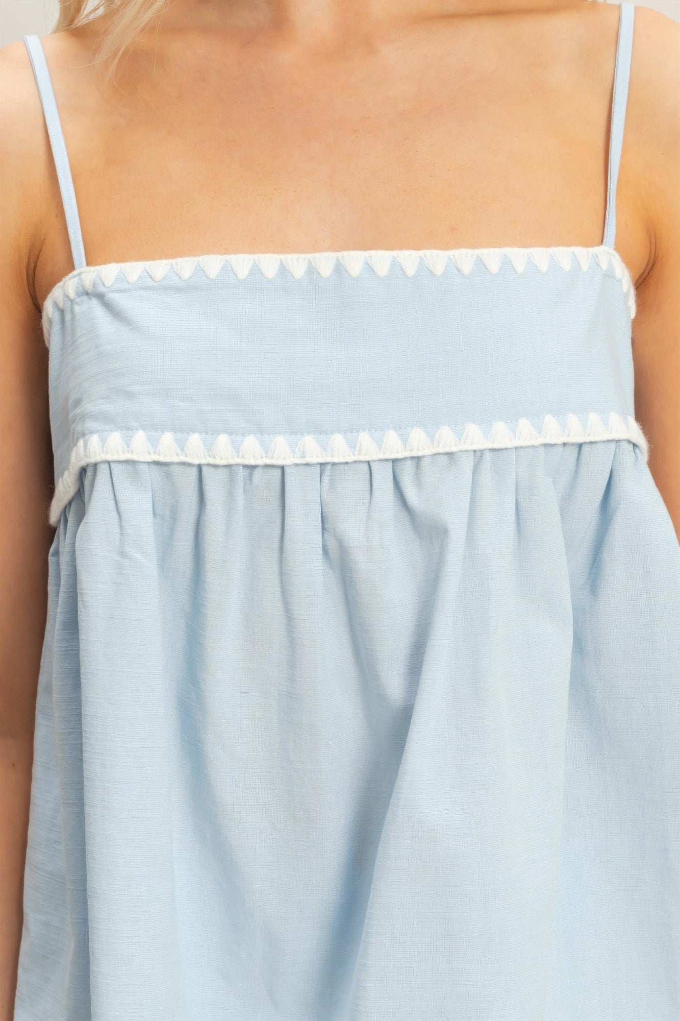 Close-up light blue babydoll top: smocked bodice and zigzag trim along top seam