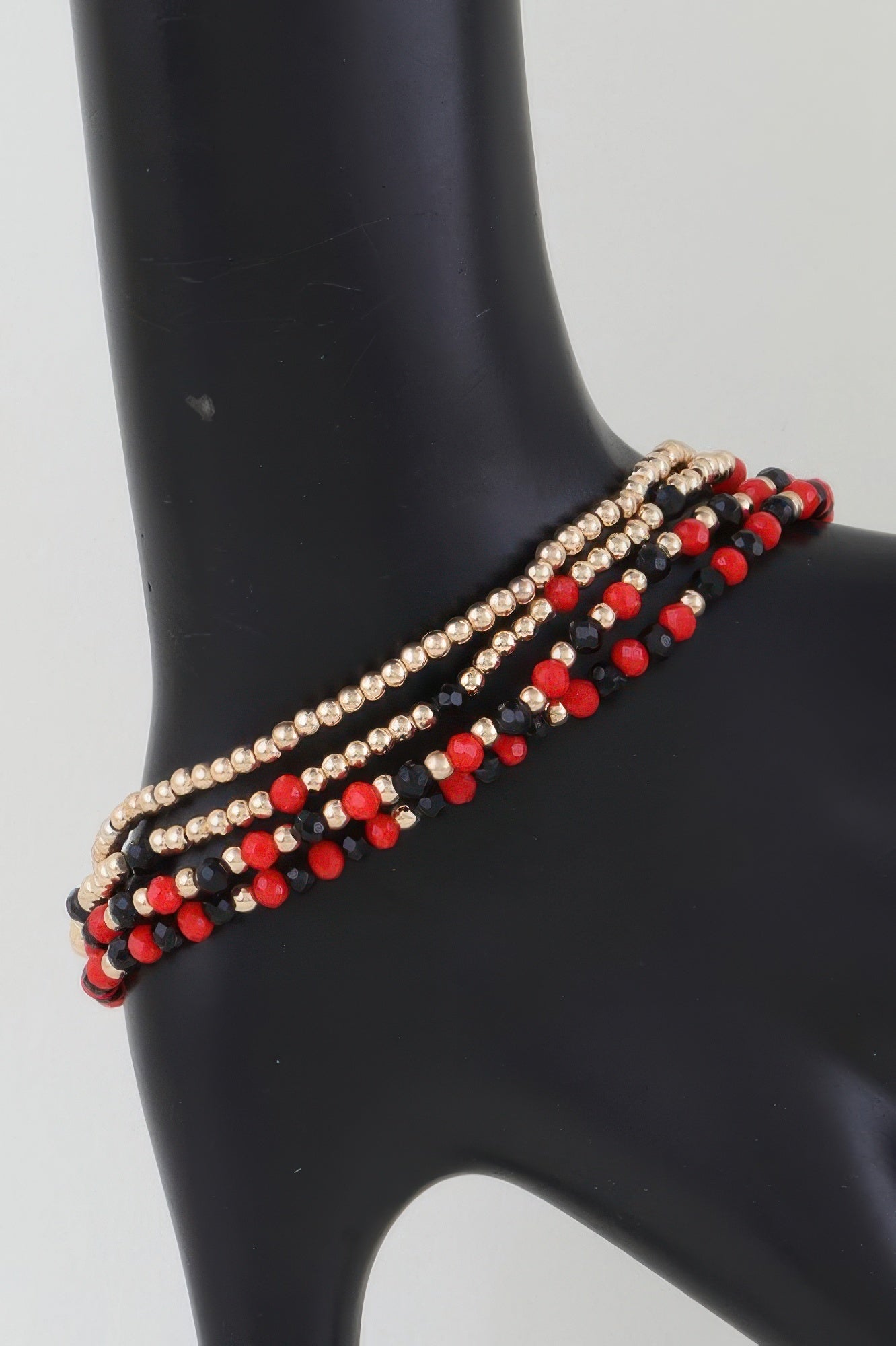 Alternating stone beaded bracelet with gold beads and red accents on a dark base