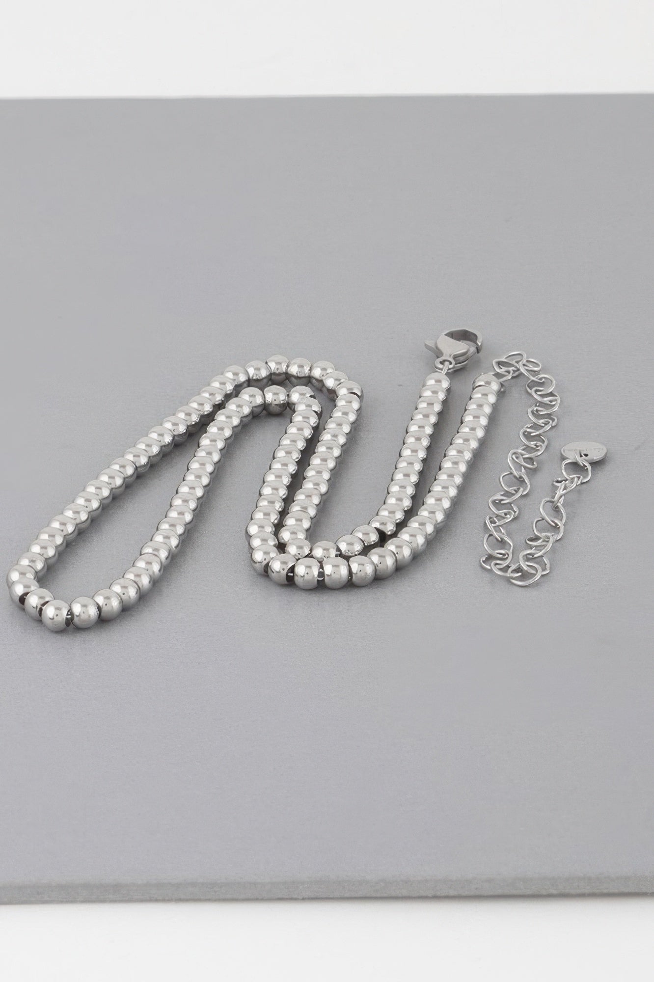 Silver beaded necklace set with clasp and chain links, laid flat