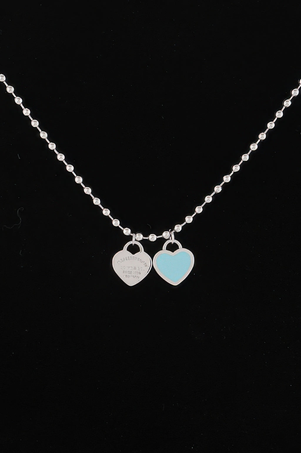 Heart pendant necklace close-up: silver chain with two heart charms, one light blue