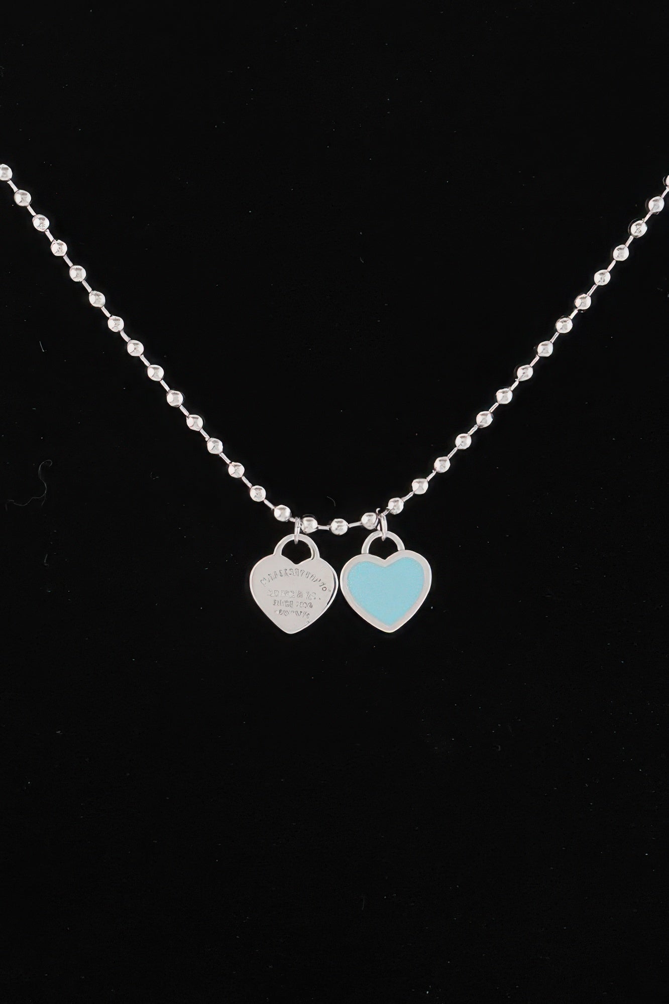 Heart pendant necklace close-up: silver chain with two heart charms, one light blue