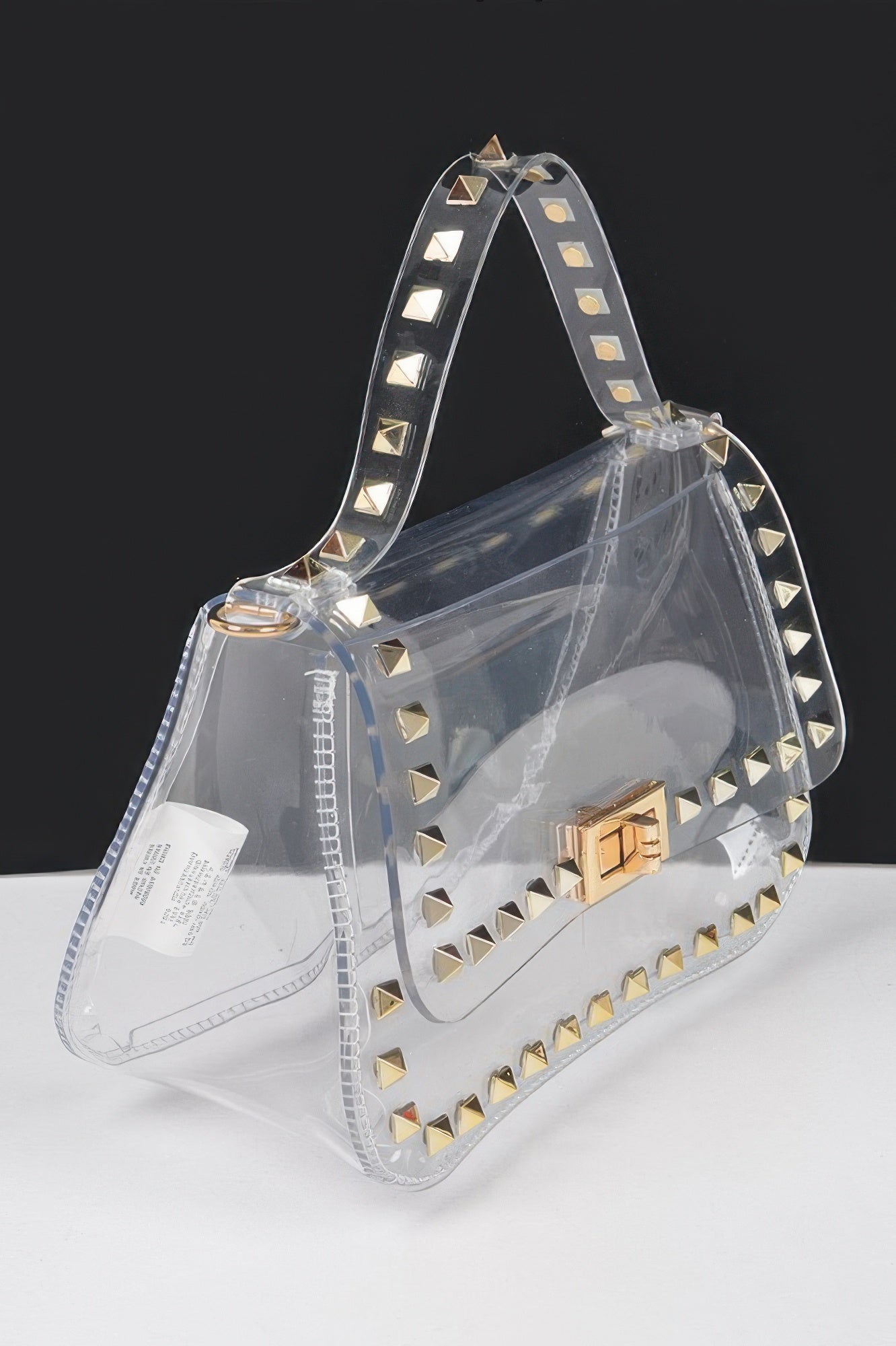 Transparent handbag with gold stud trim, top handle, and gold buckle clasp
