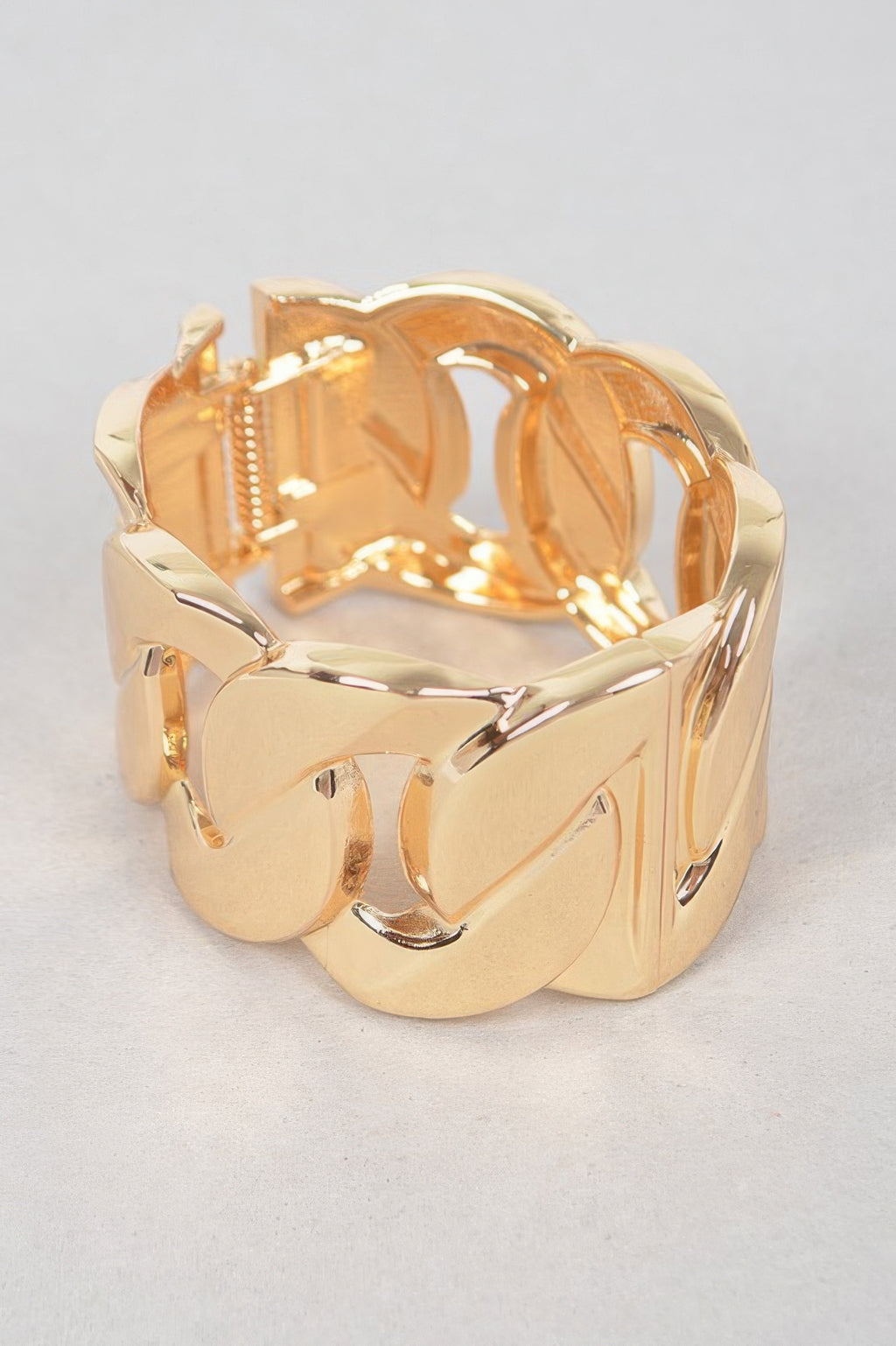 Wide gold metal chain bracelet, close-up of curved links with polished reflective edges