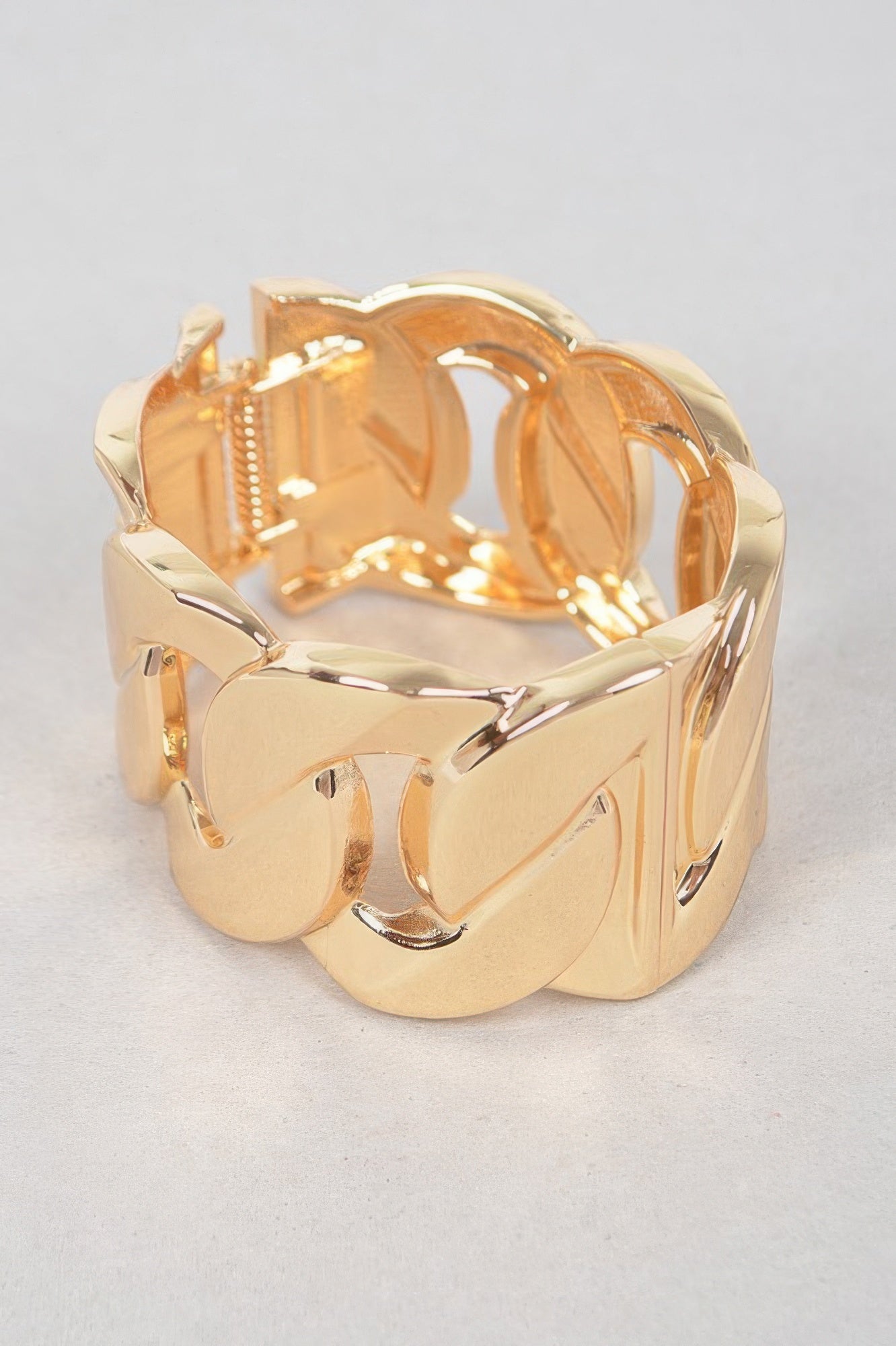 Wide gold metal chain bracelet, close-up of curved links with polished reflective edges