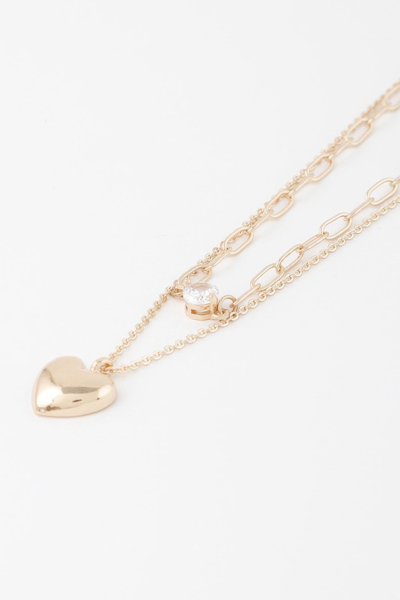 Close-up gold heart pendant necklace with small clear-stone heart charm on chain