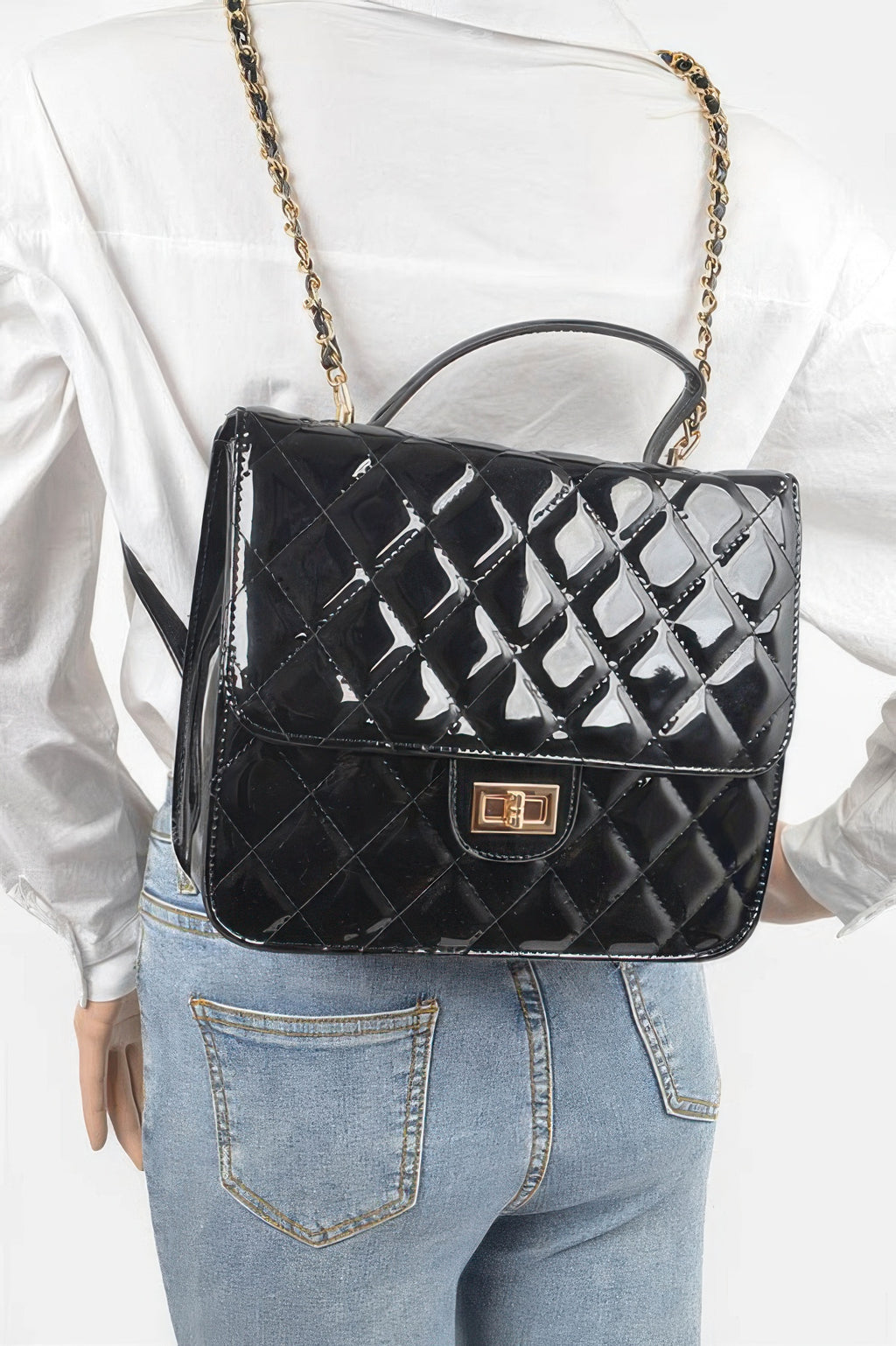 Black quilted enamel backpack on person, with top handle and gold chain shoulder strap