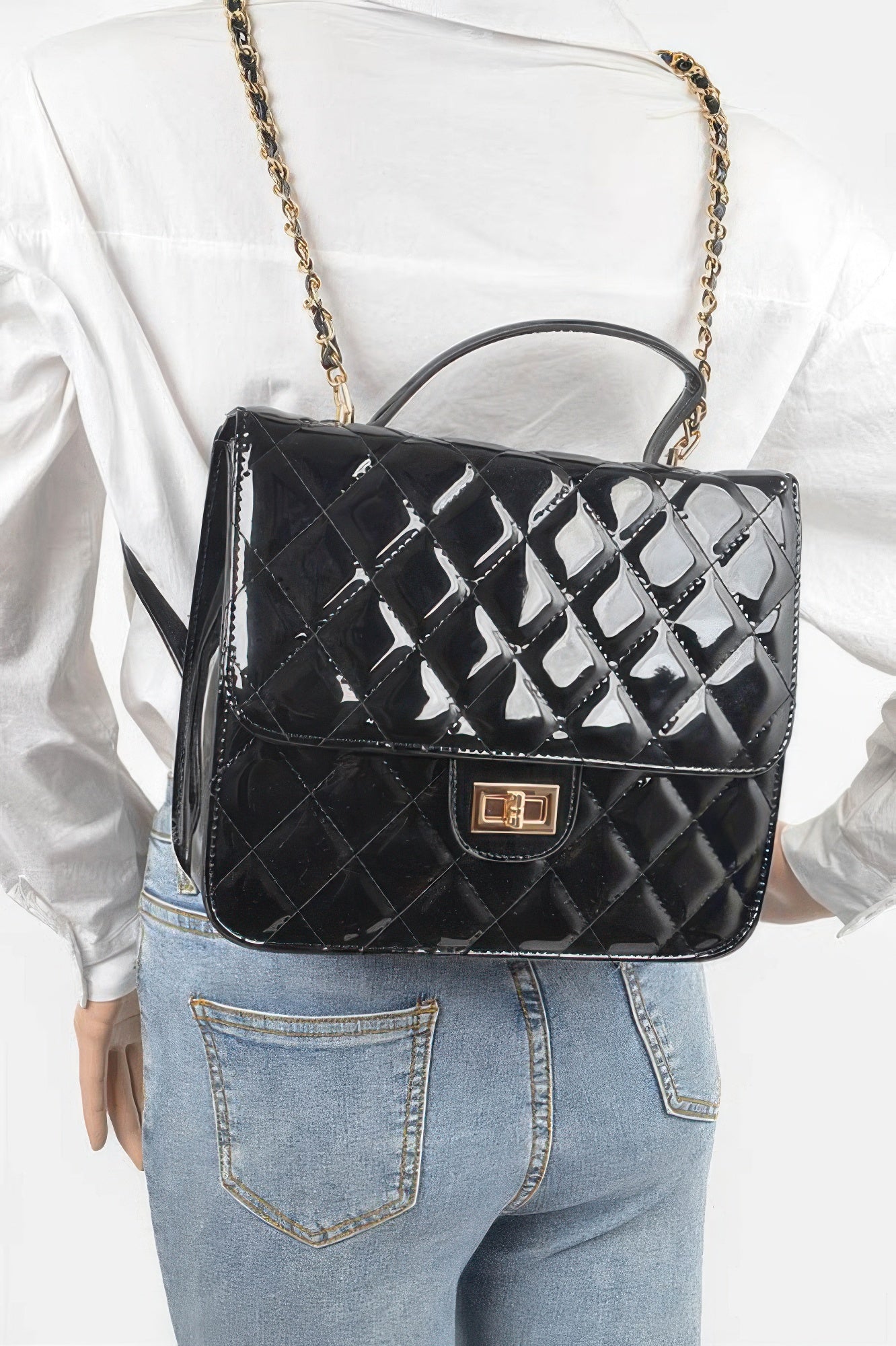 Black quilted enamel backpack on person, with top handle and gold chain shoulder strap