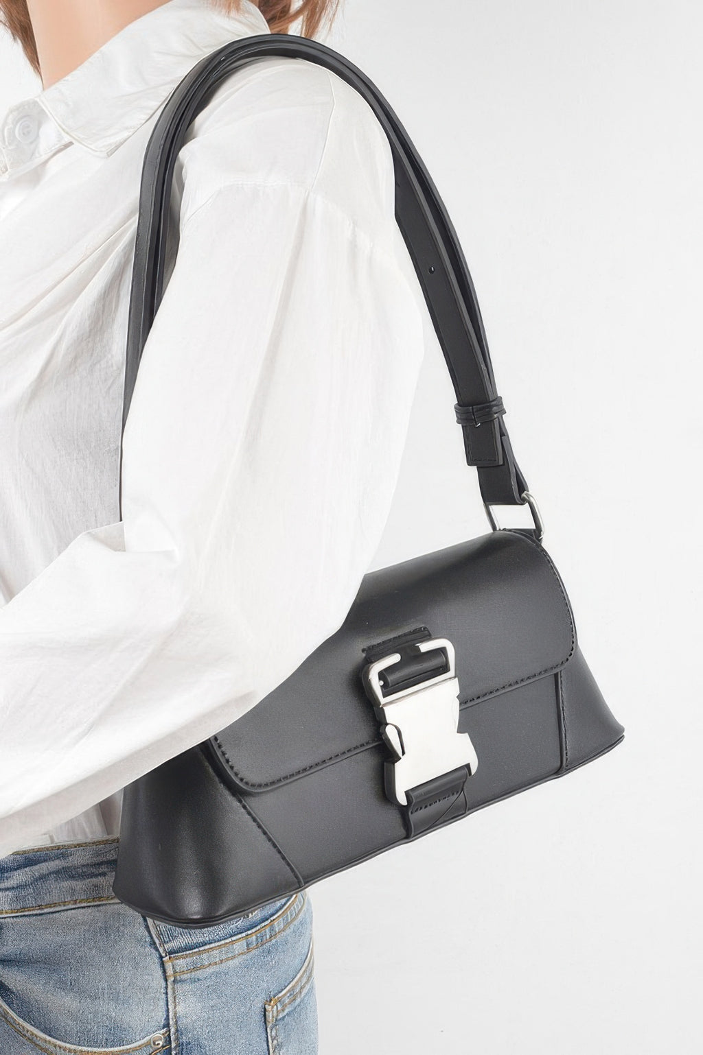 Black faux leather shoulder bag worn crossbody, metal buckle front
