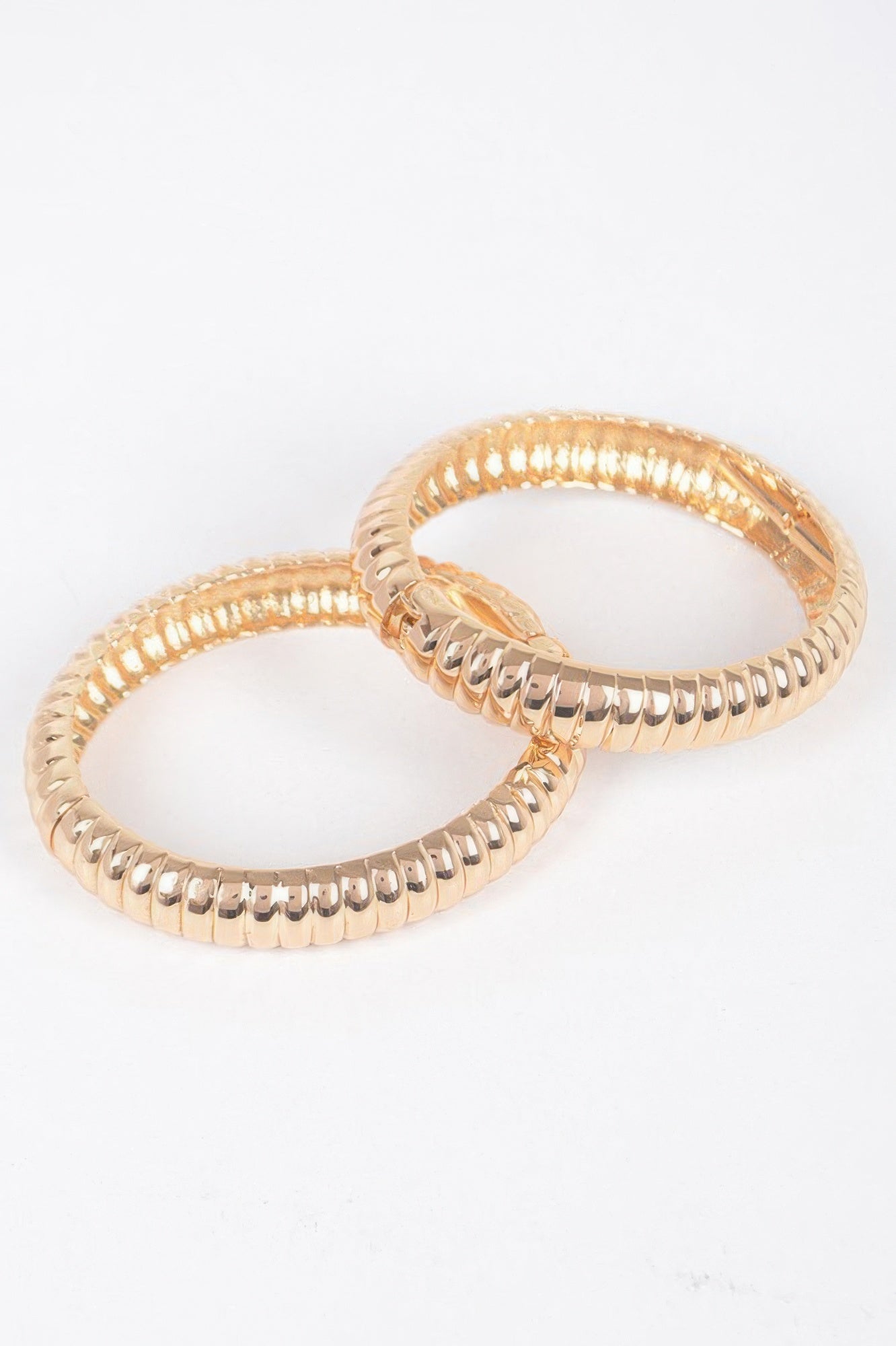 Gold bangle pair with oval hoops and beaded ribbed edges, clasp visible at side.