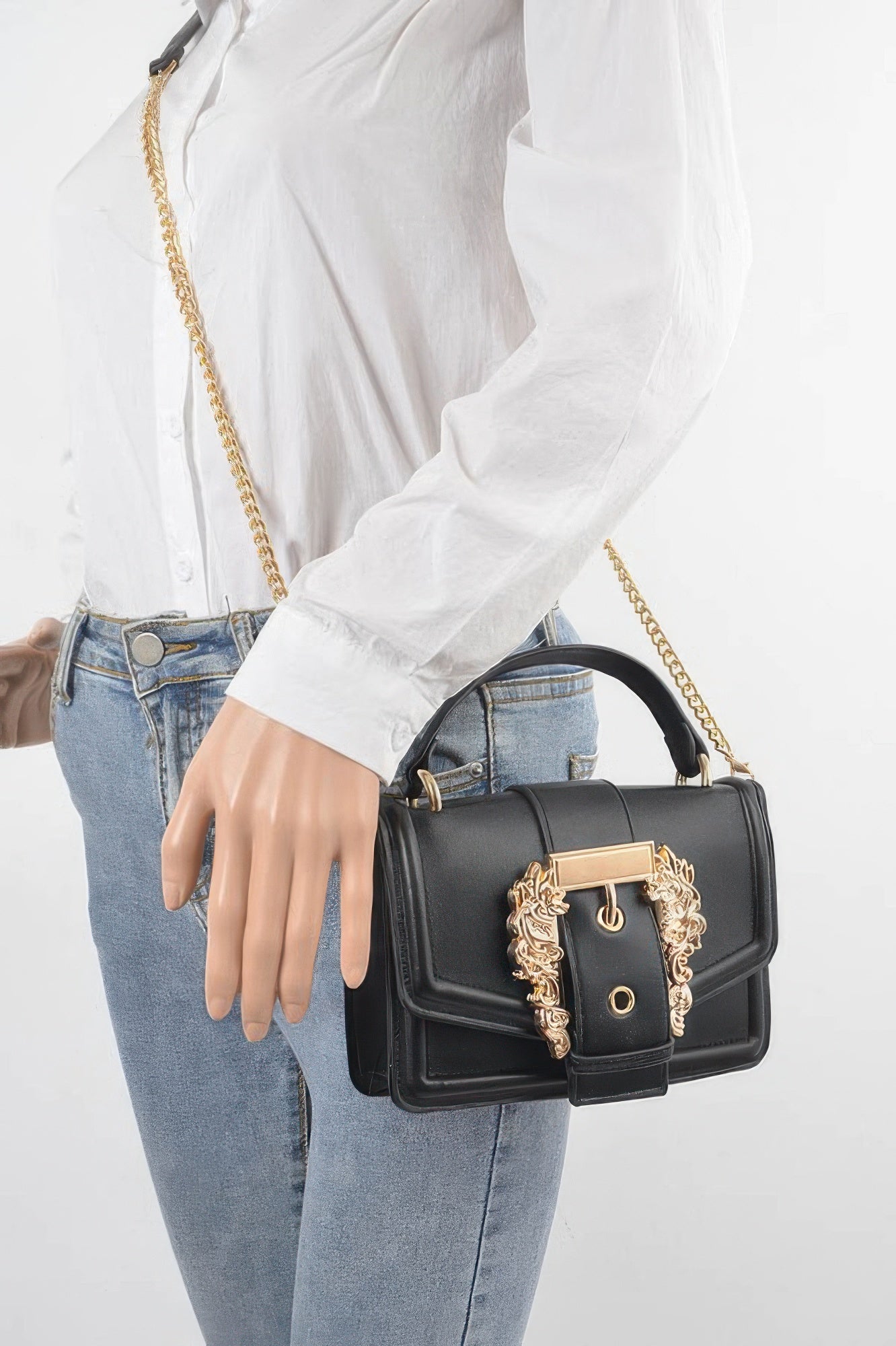 Black vegan clutch held by model, gold chain shoulder strap and ornate front clasp