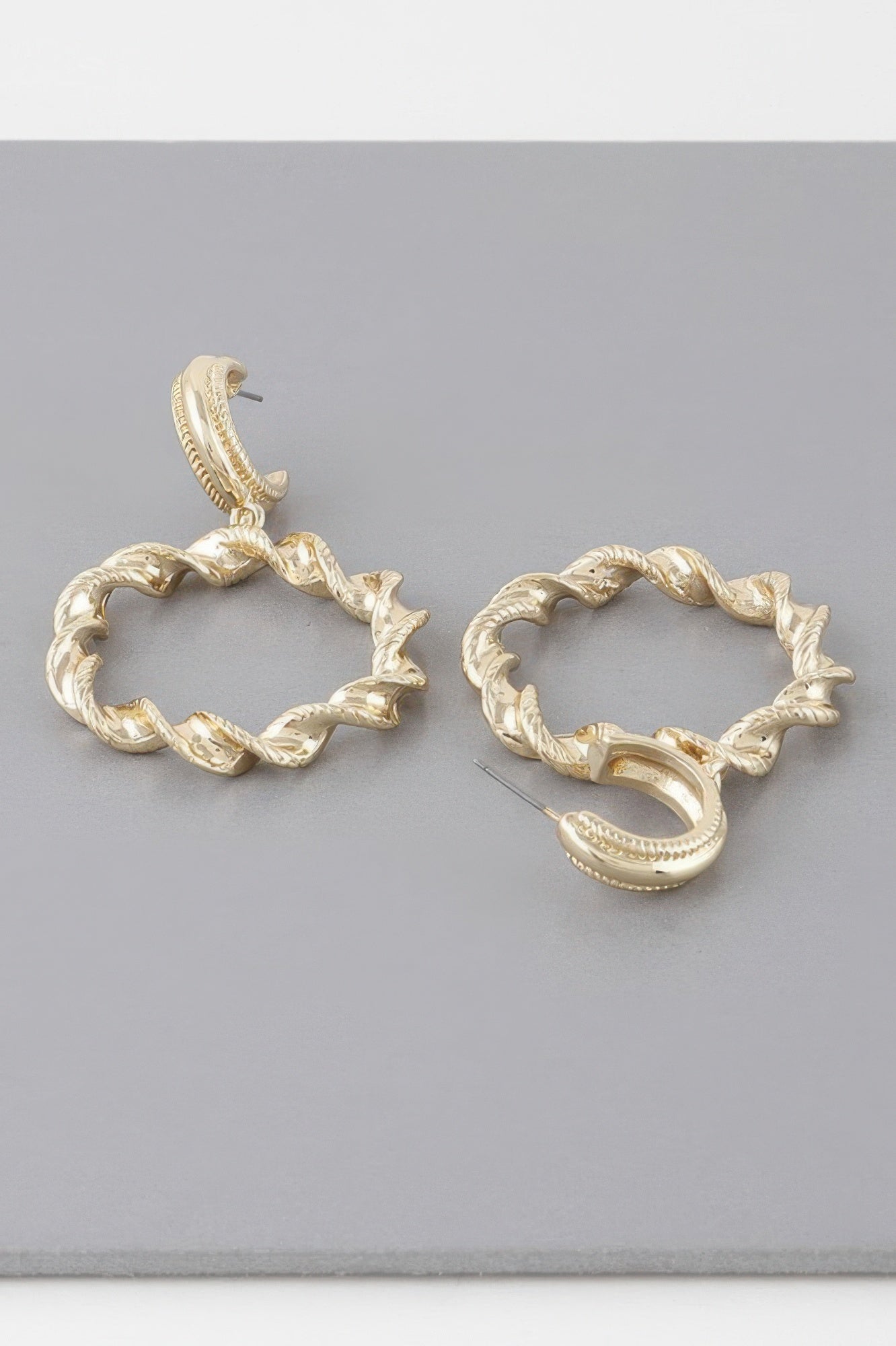 Gold twisted hoop drop earrings, close view of circular hoops and dangling clasp