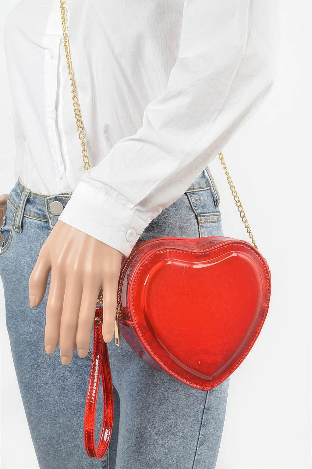 Red heart crossbody bag worn at side with gold chain strap over denim