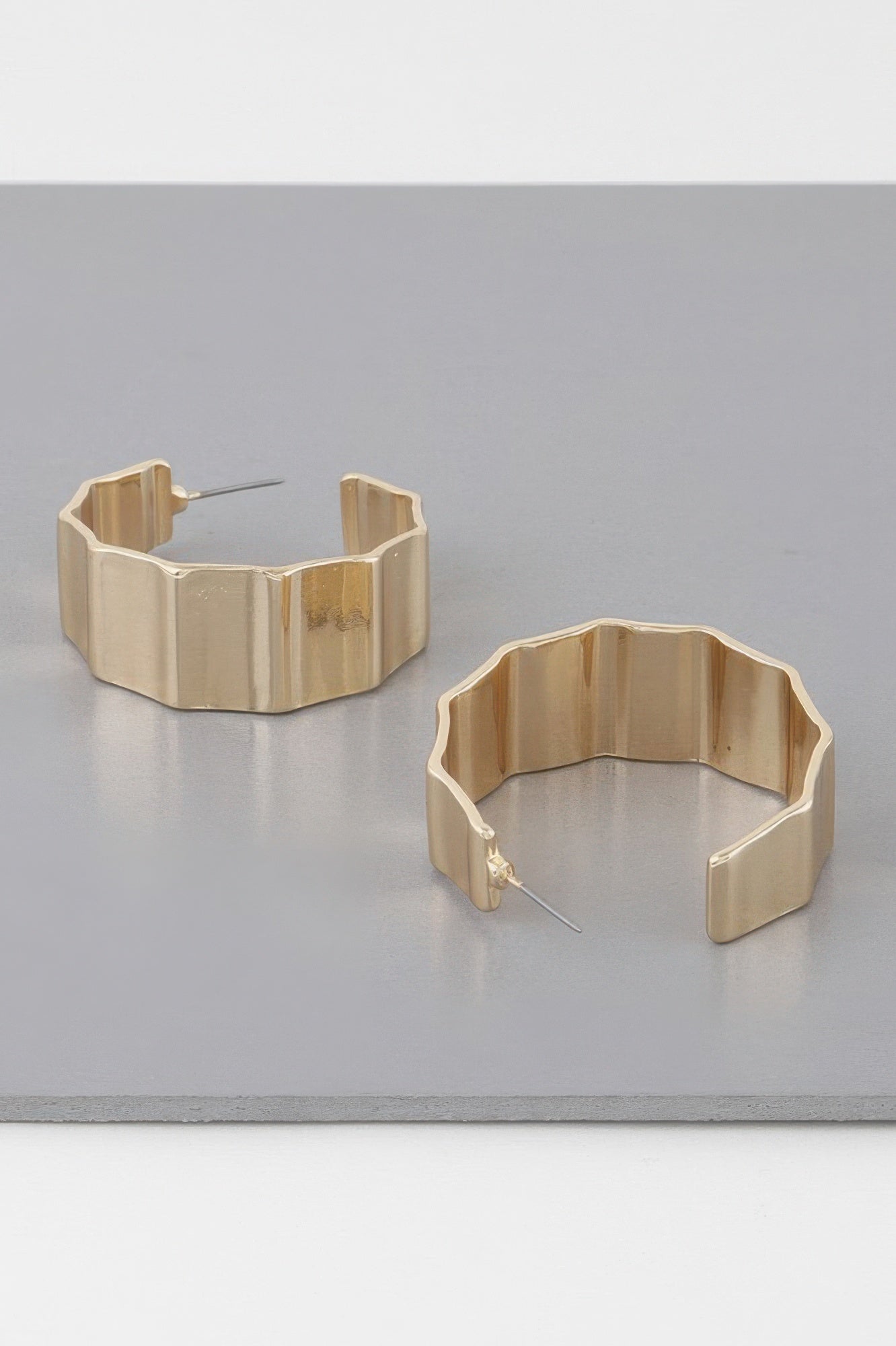 Gold ribbed hoop earrings shown from side, open C-shaped metal band