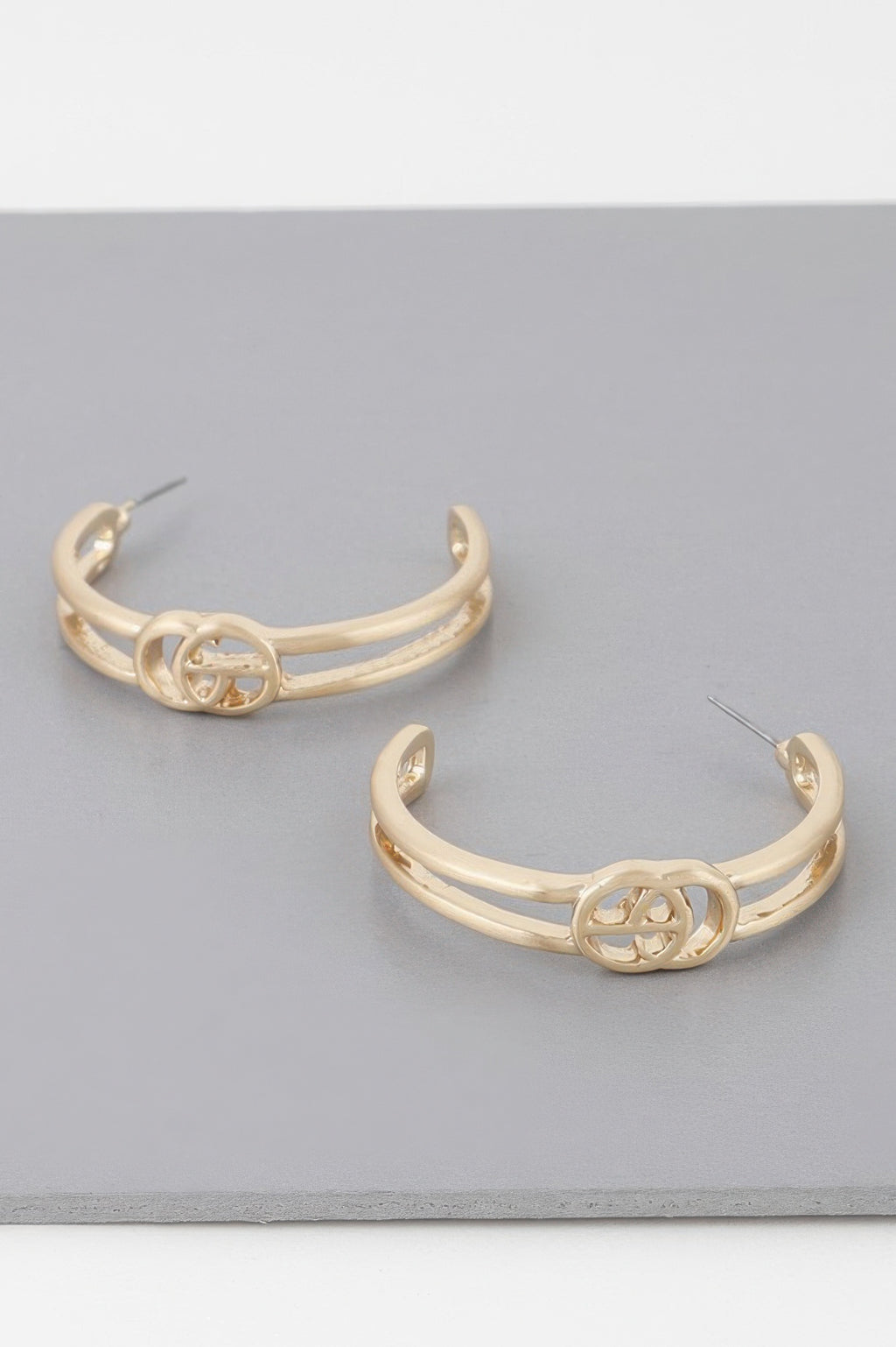 Gold Cg hoop earrings with central emblem detail, front view.