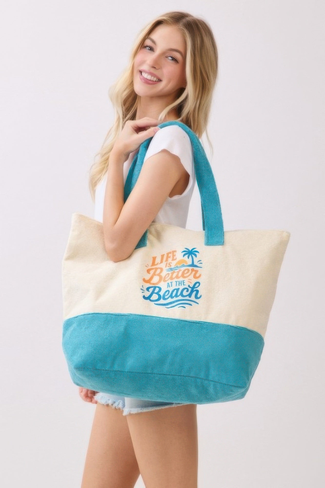 Terry tote de playa con asas turquesa y bolsa inferior azul, texto “Life is Better at the Beach”.