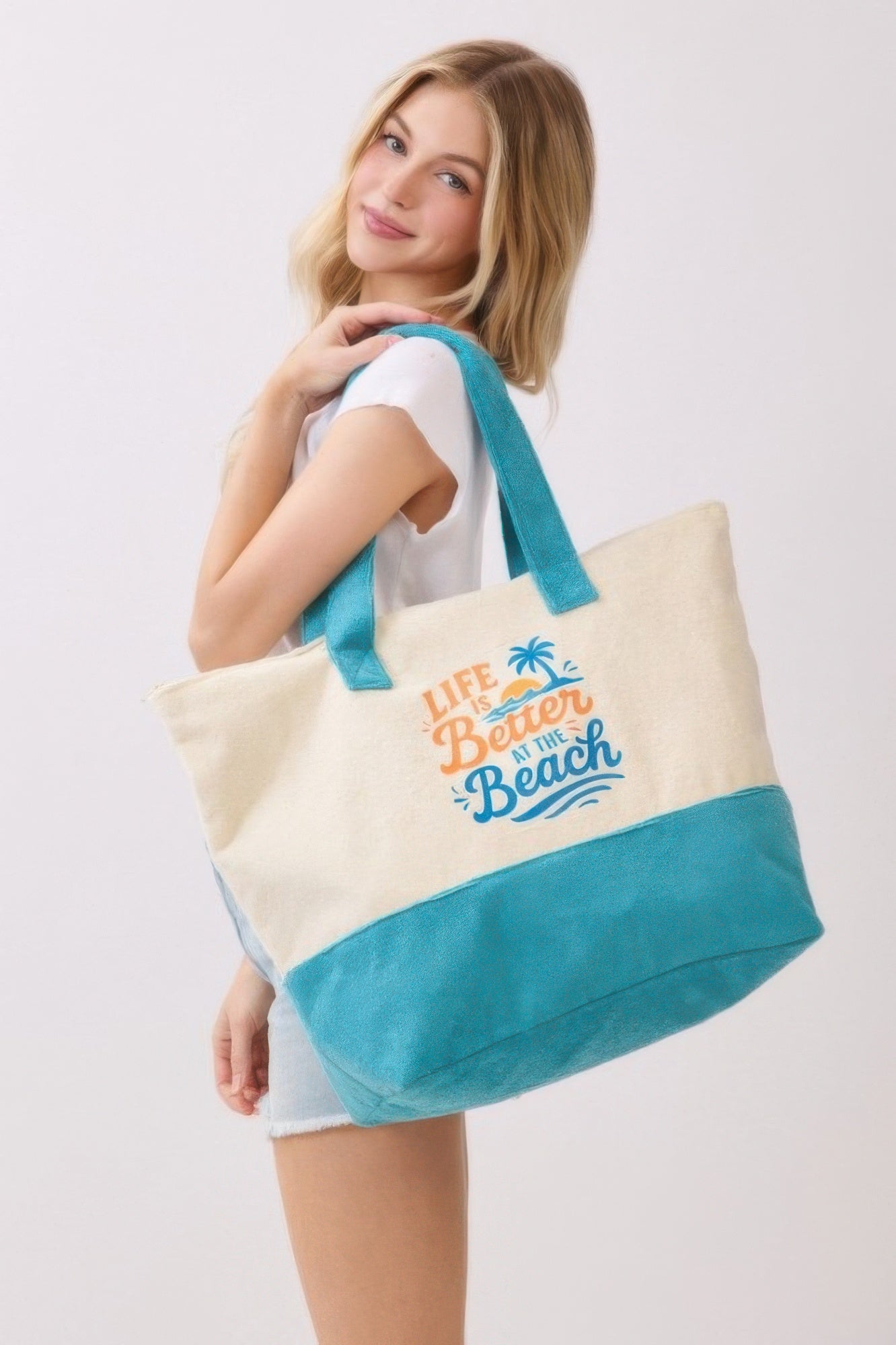 Bolso tote de playa crema con base azul y asa turquesa, con gráfico de palmera y texto.