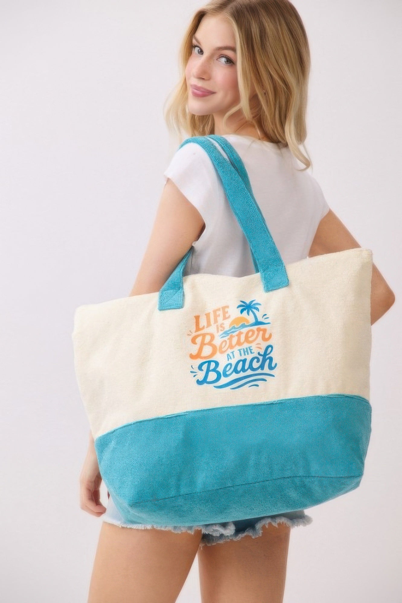 Tote con asas turquesa y fondo azul, diseño “Life is Better at the Beach” en el centro.