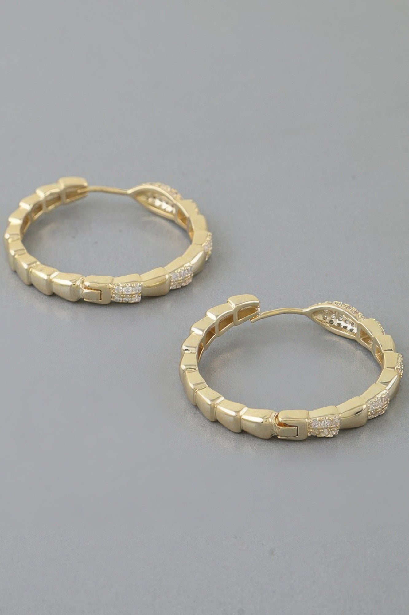 Gold hoop earrings with snake scale texture and small crystal accents
