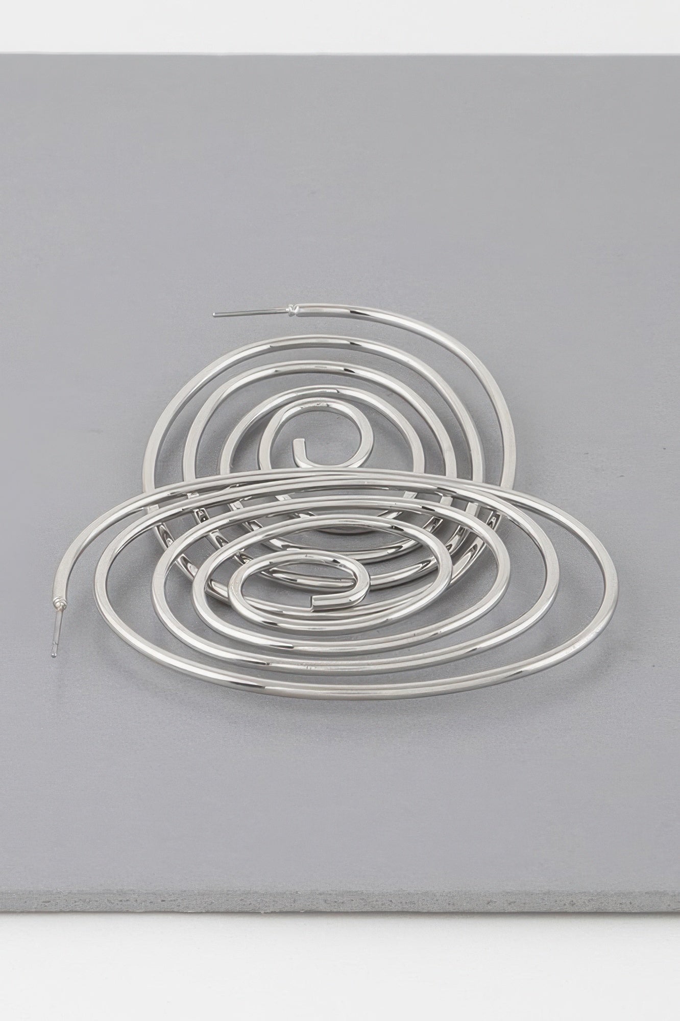 Abstract swirl stud earrings in silver, layered circular spiral design.