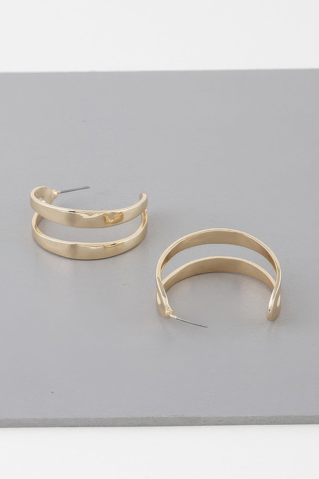 Gold open hoop earrings, overlapping curved hoops with small charm detail