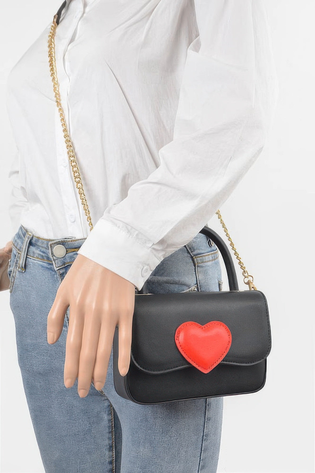 Black vegan top-handle bag with red heart flap and gold chain worn crossbody