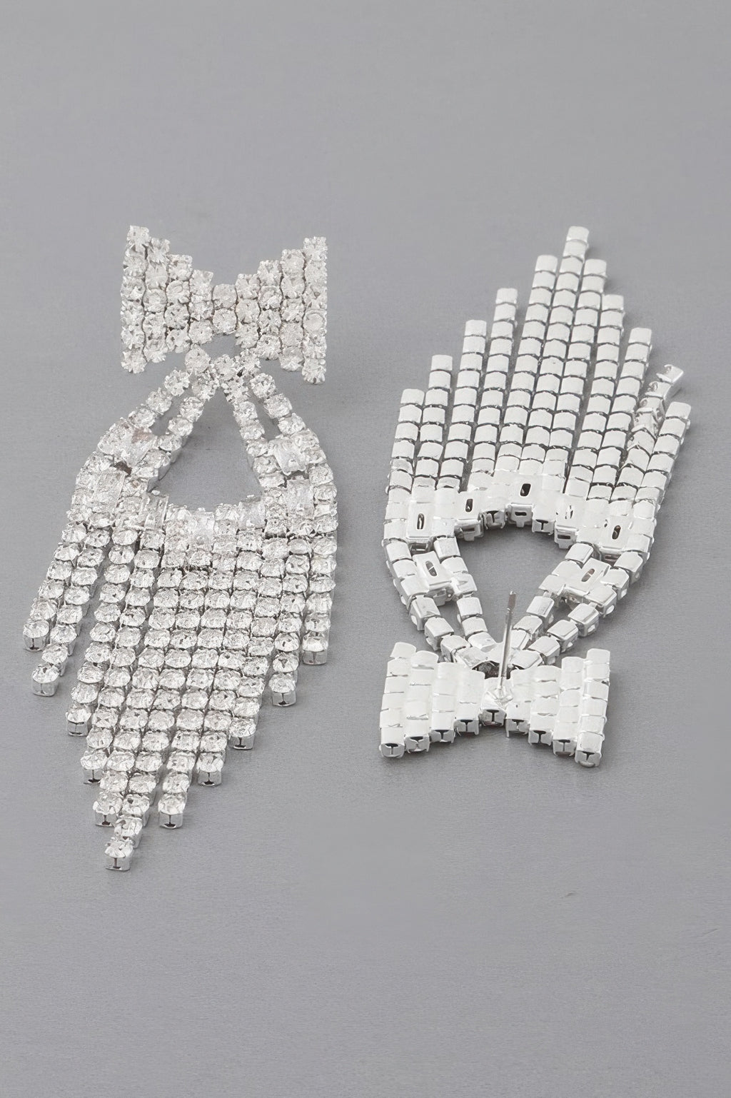 Rhinestone ribbon drop earrings laid flat—bow detail, grid of round stones, fringe drops