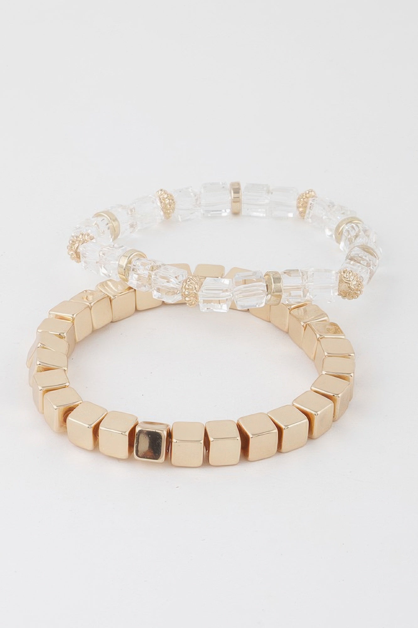 Stacked clear-and-gold bracelets with square gold beads and clear faceted blocks, charm detail