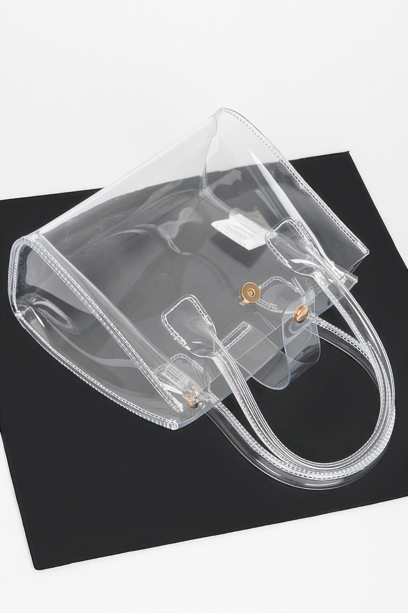 Transparent crossbody bag showing gold-tone snap closure and side handle pockets