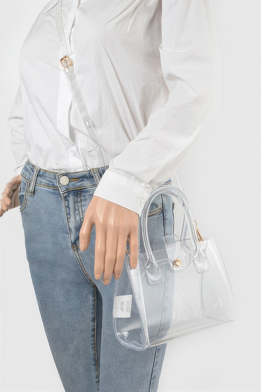 Transparent crossbody bag worn over shoulder with gold-tone clasp and top handles