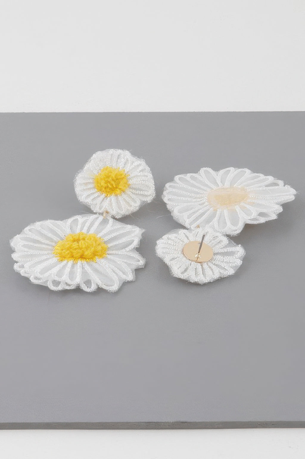 White fabric daisy flower earrings with yellow centers and visible stud backs