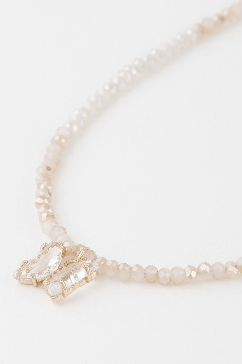 Close-up: faceted crystal butterfly charm on white-bead beaded necklace with gold clasp