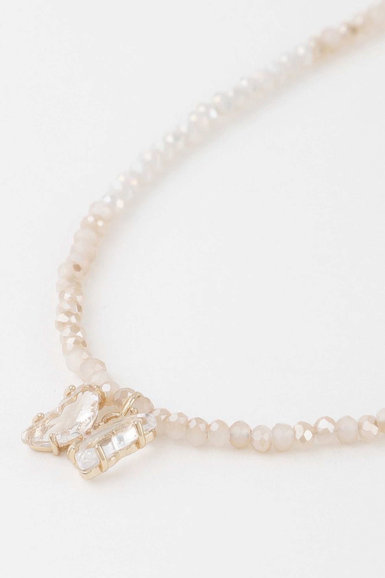 Close-up: faceted crystal butterfly charm on white-bead beaded necklace with gold clasp