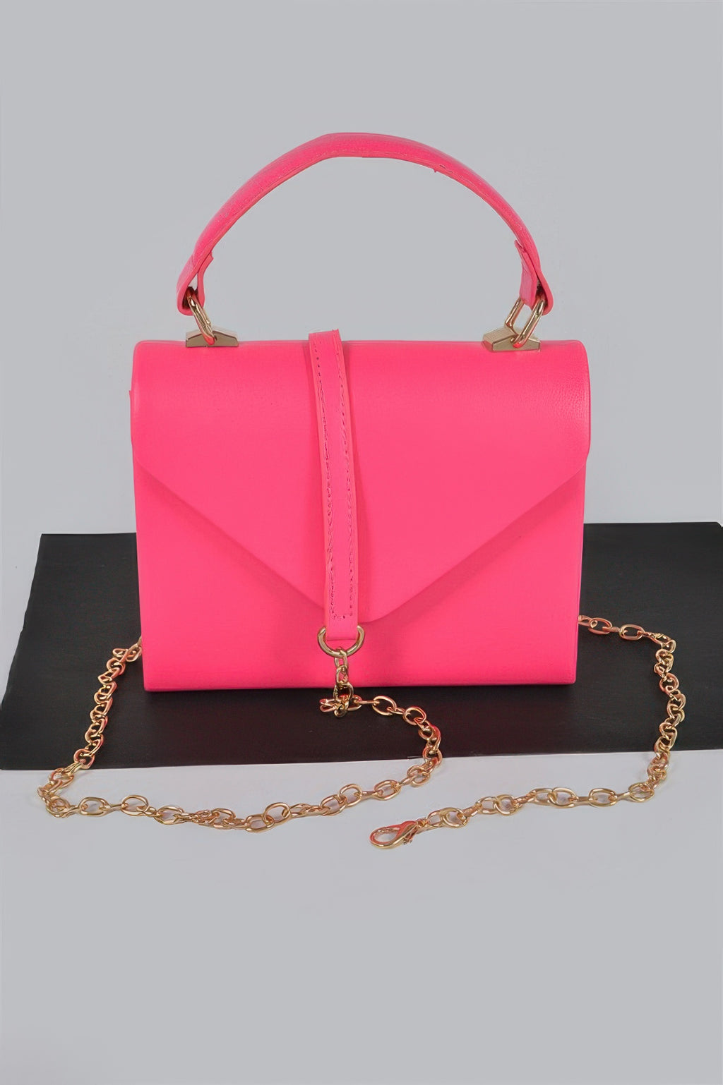 Neon pink boxy clutch with top handle, flap front, and gold chain strap