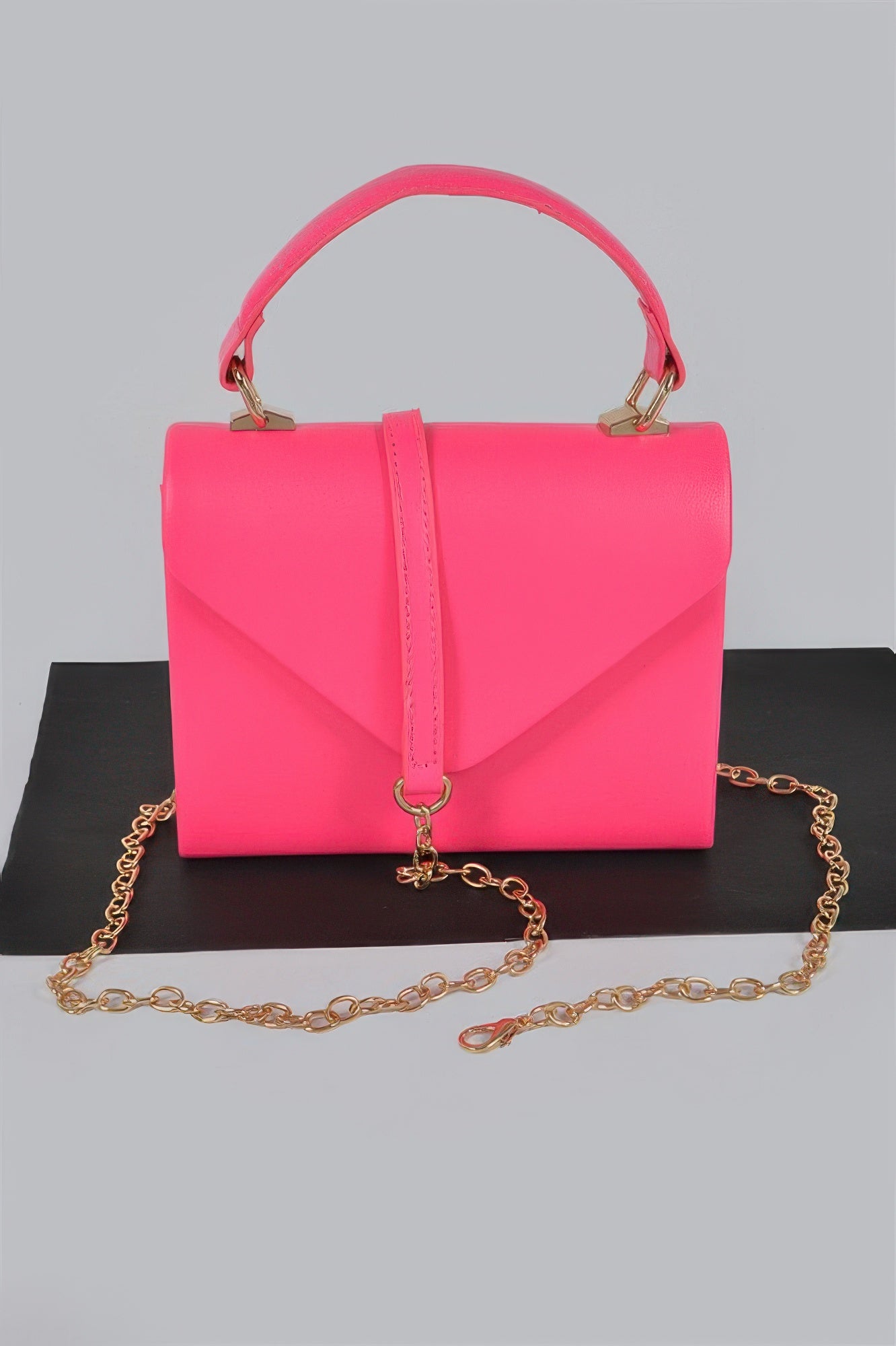 Neon pink boxy clutch with top handle, flap front, and gold chain strap