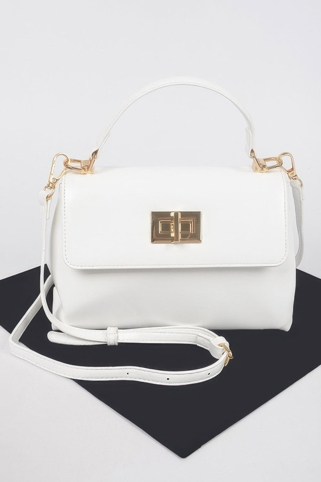 White faux leather flap bag with gold clasp; top handle and crossbody strap