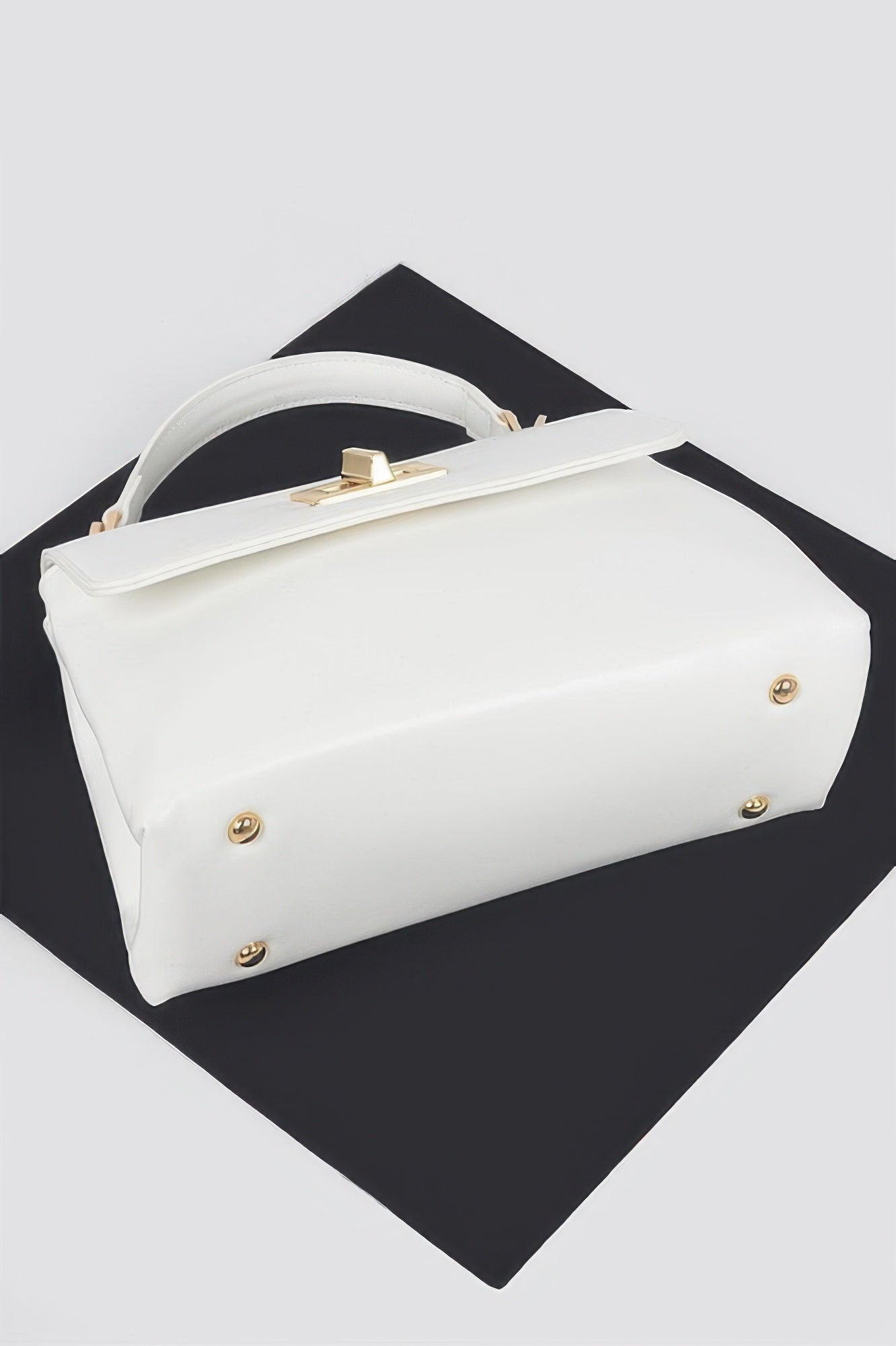 White faux leather flap bag with top handle, gold studs, and front hardware