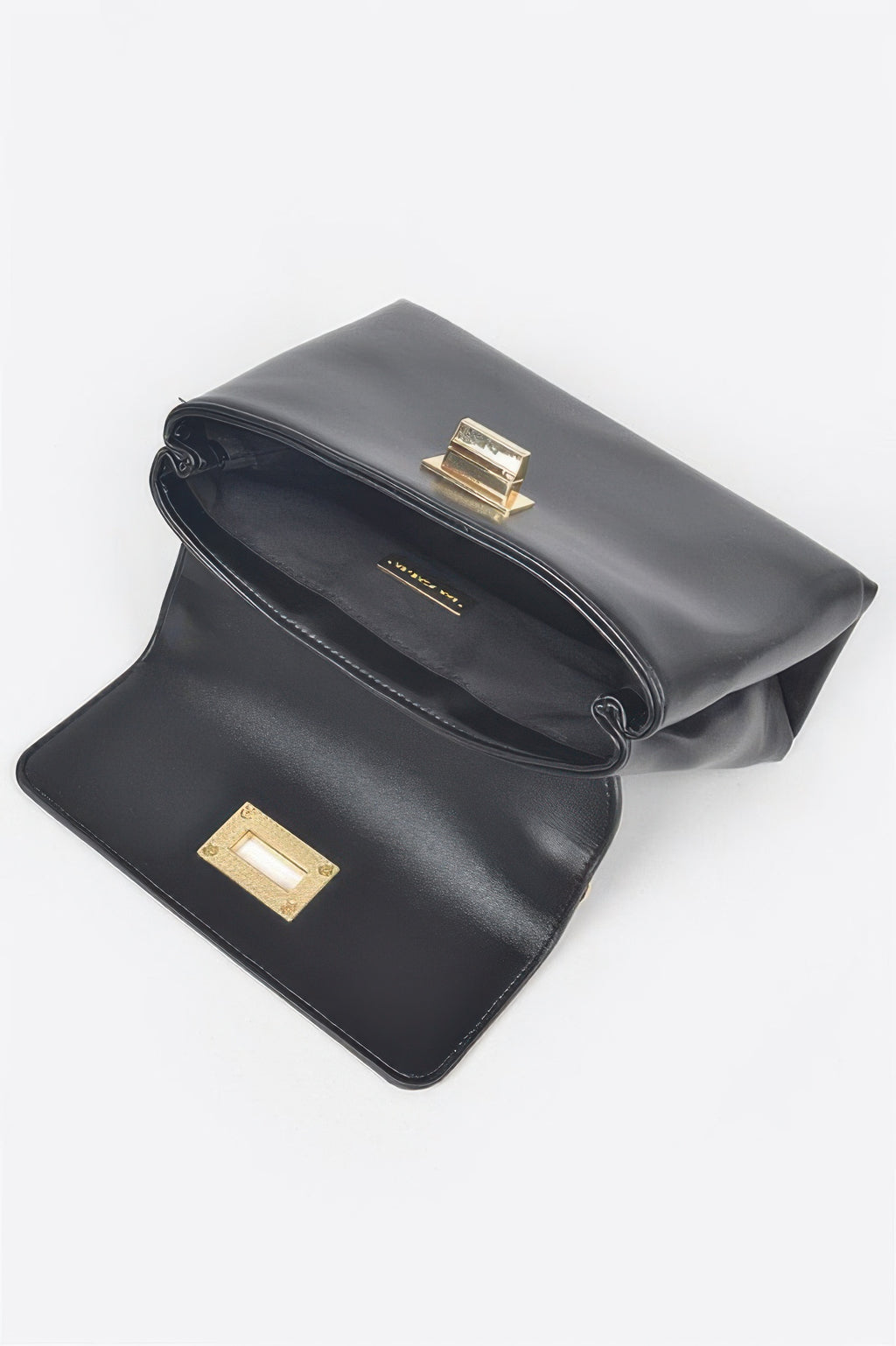 Black faux leather flap bag with gold clasp, rolled flap, and interior pocket flap