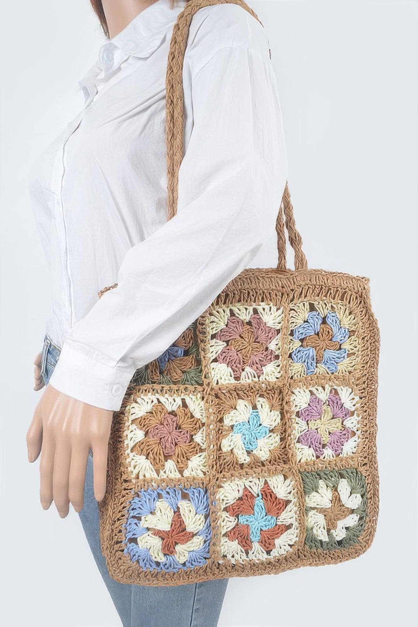 Faux straw tote bag worn on shoulder, multicolor floral crochet squares on khaki base