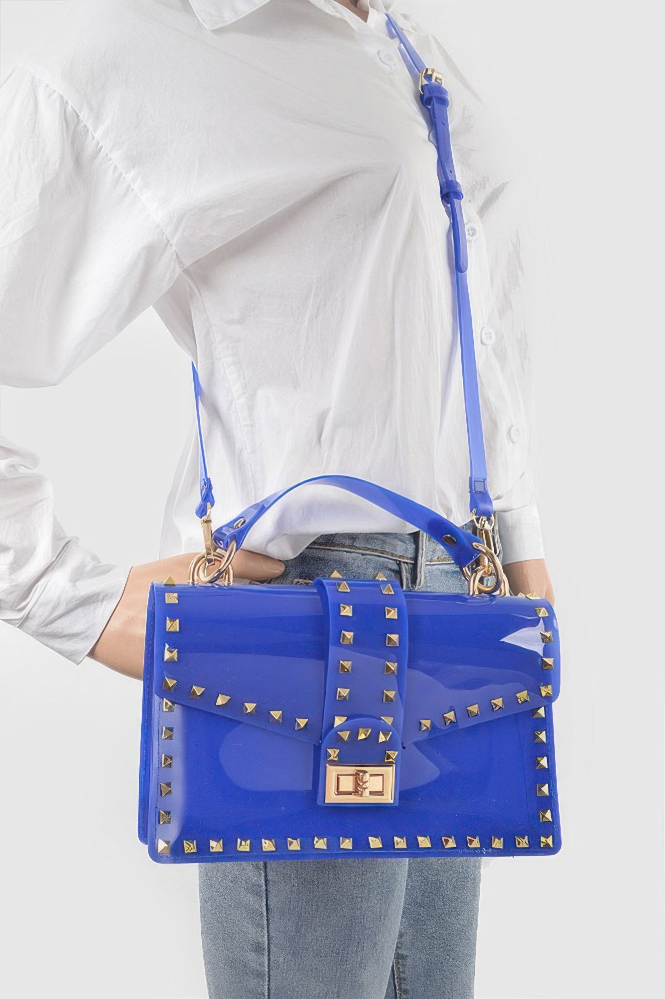 Cobalt transparent clutch worn with crossbody strap, gold stud trim, front lock