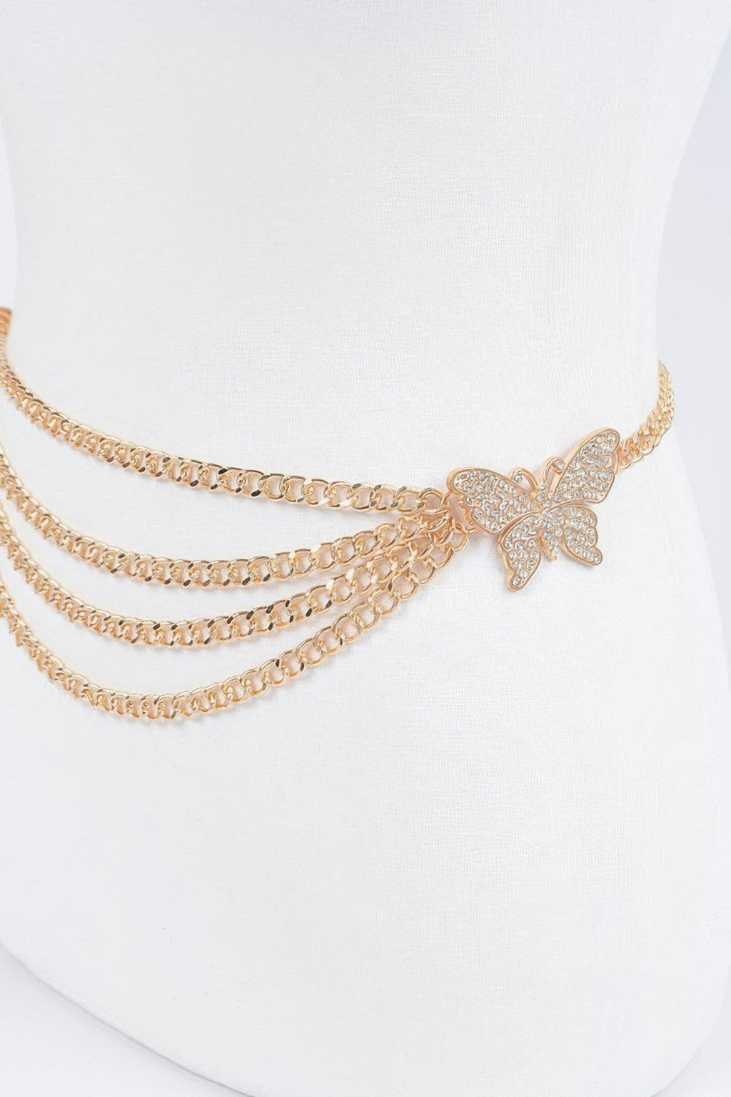 Close-up: gold butterfly buckle on layered chain belt with three rows