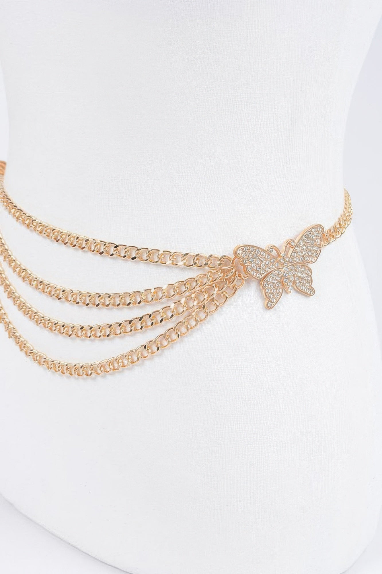 Close-up: gold butterfly buckle on layered chain belt with three rows