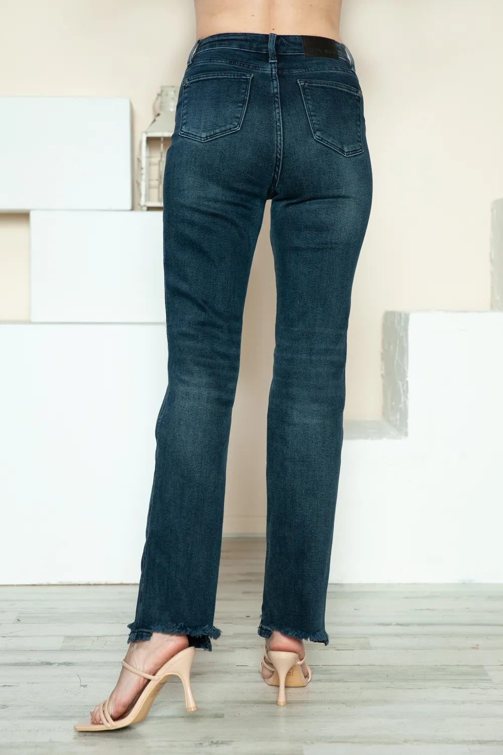Rear view of dark blue straight jeans with raw hem and back patch pockets