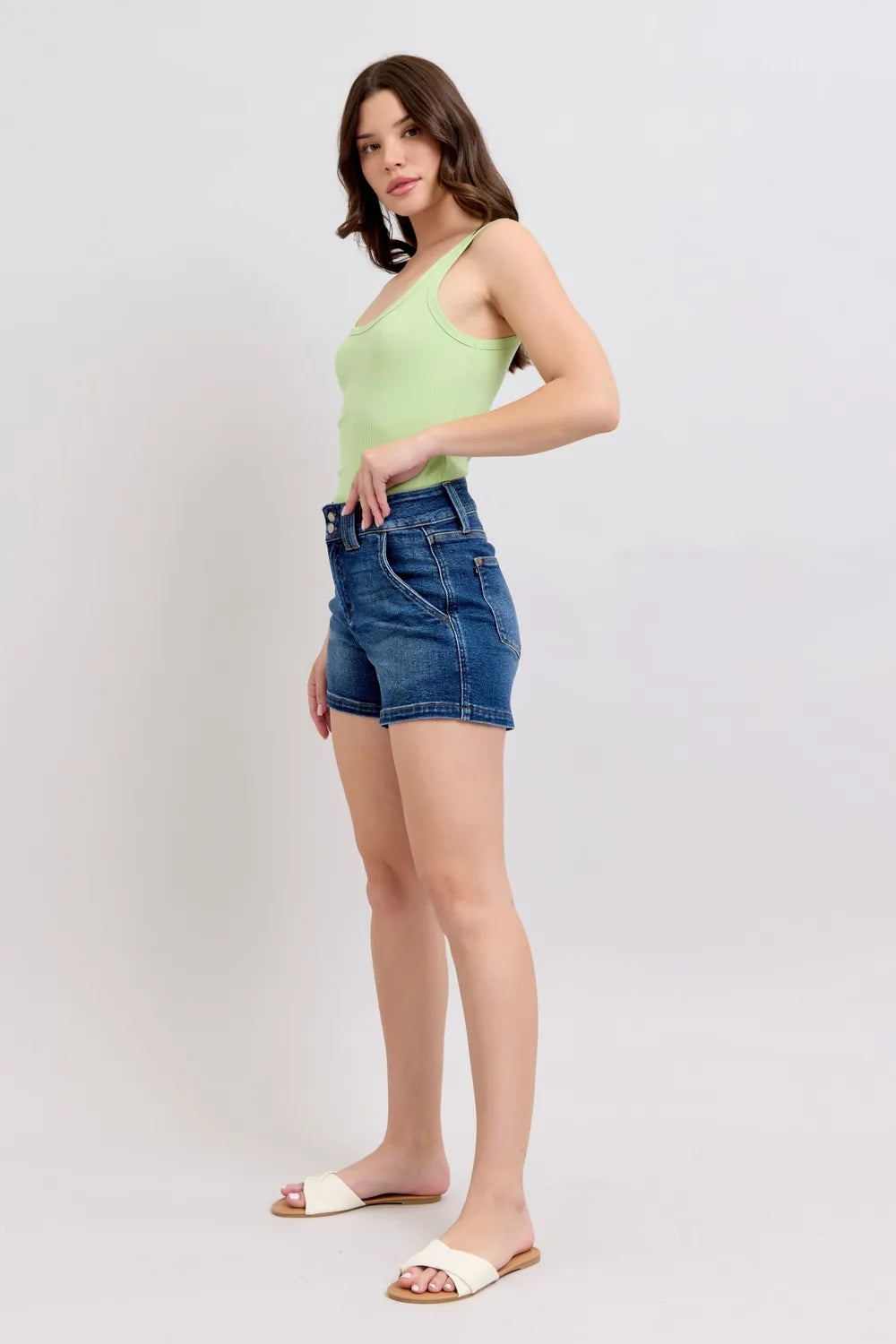 Side view of dark denim shorts with double-button waistband and curved seams