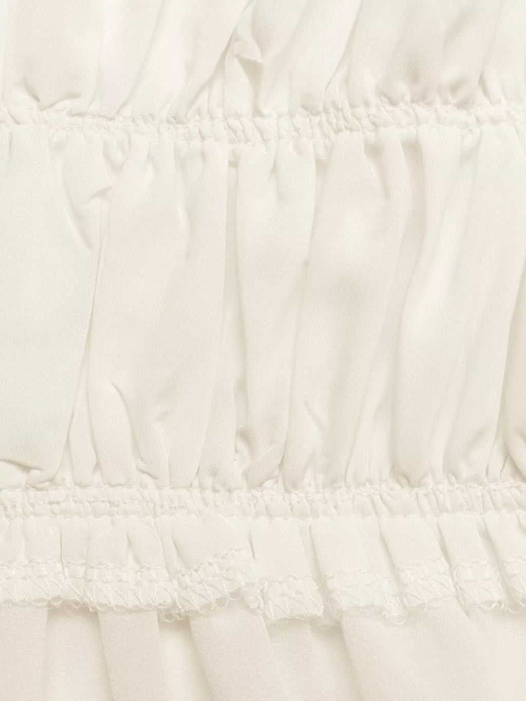 Close-up of white smocked waist and gathered tiered peplum layers