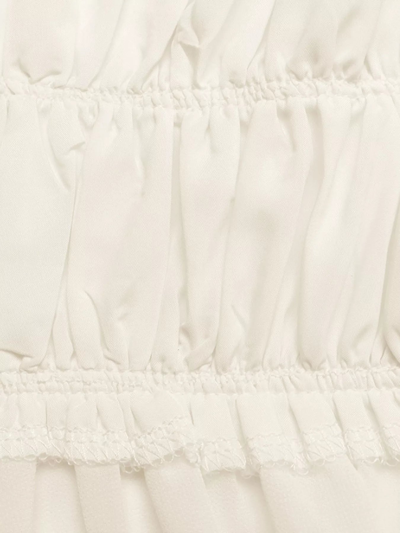 Close-up of white smocked waist and gathered tiered peplum layers