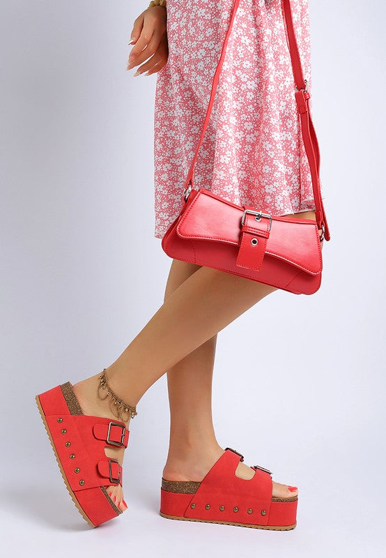 Red flatform sandals with stud trim and two buckled straps worn on model