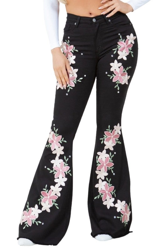 Black bell-bottom jeans with pink and white floral embroidery on front legs